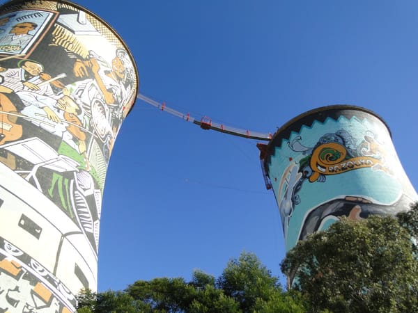 Soweto cooling towers with a bungee jumping bridge between them against a blue sky.